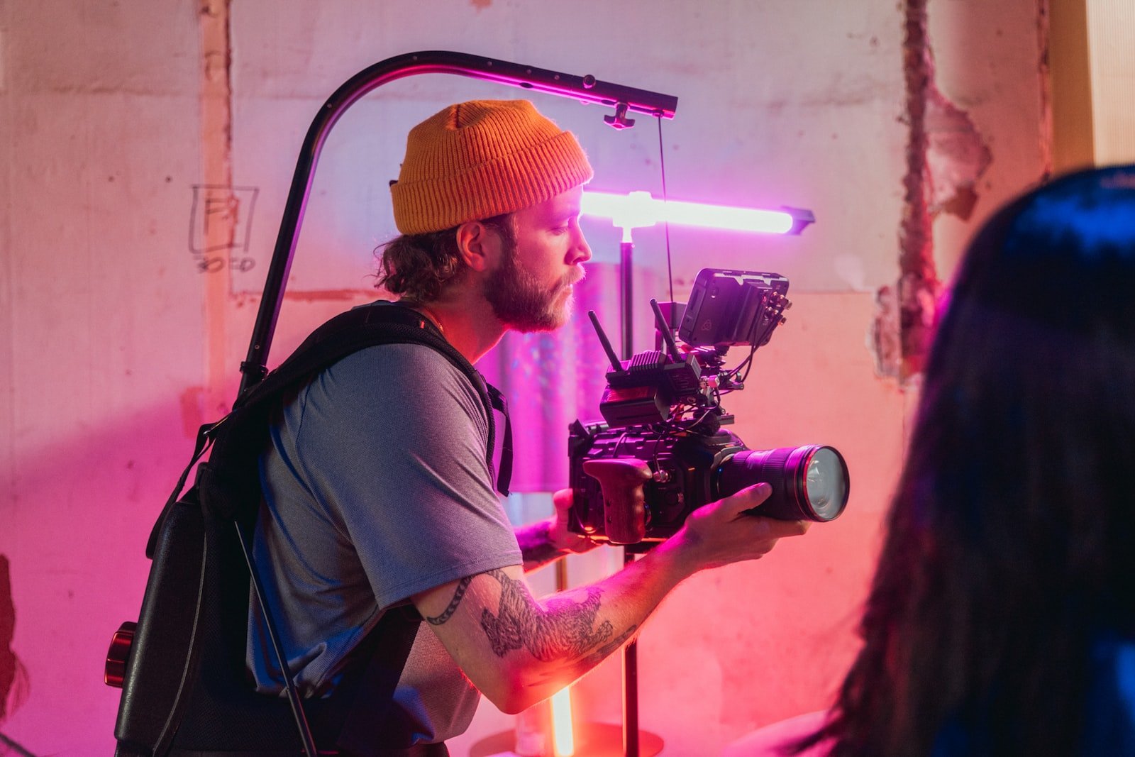 man in brown t-shirt and orange knit cap holding black video camera