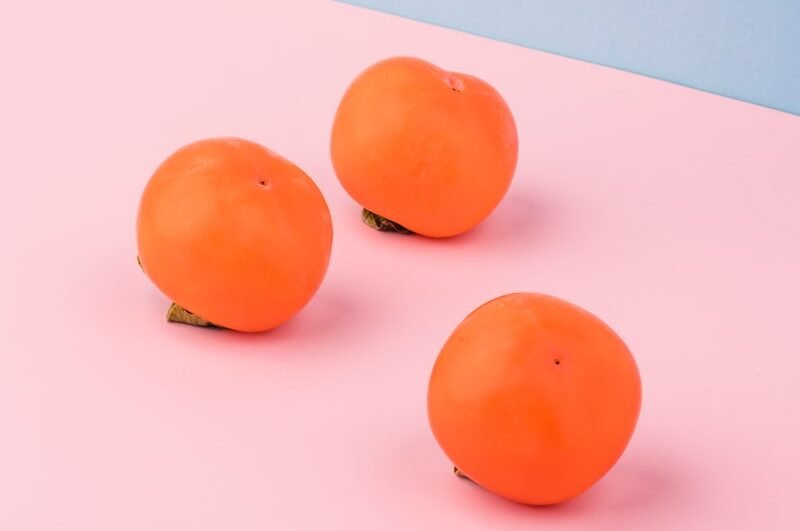 three orange fruits on pink surface