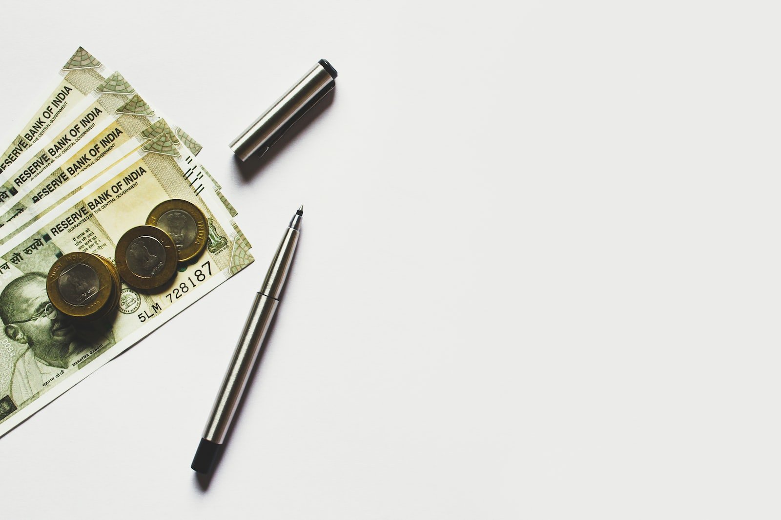 gray pen beside coins on Indian rupee banknotes